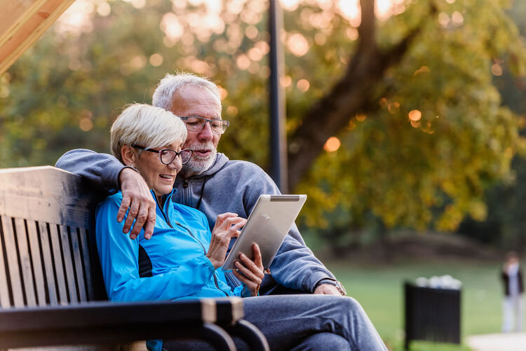Older couple sitting on a park bench looking at a tablet together
