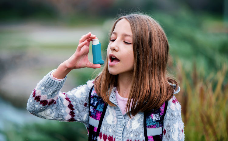 Girl using an asthma inhaler outdoors