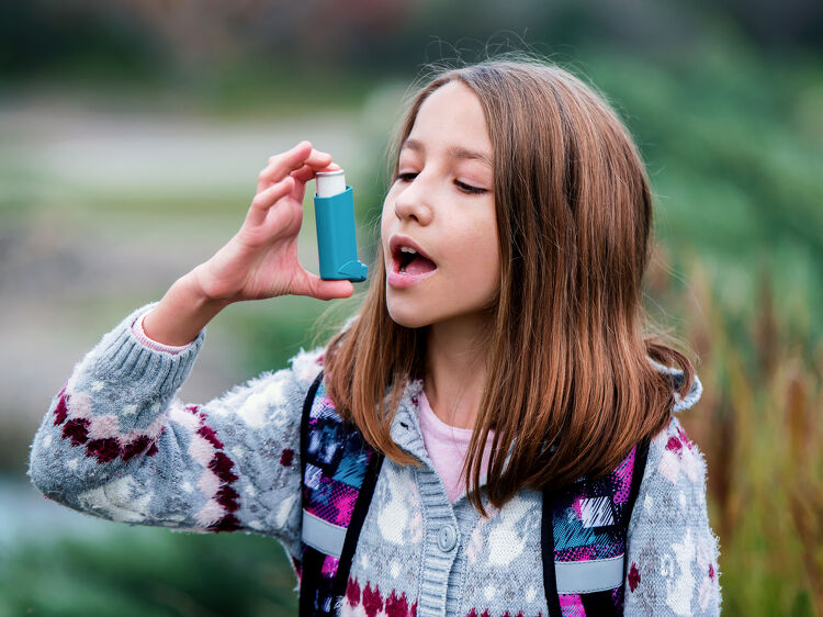 Girl using an asthma inhaler outdoors