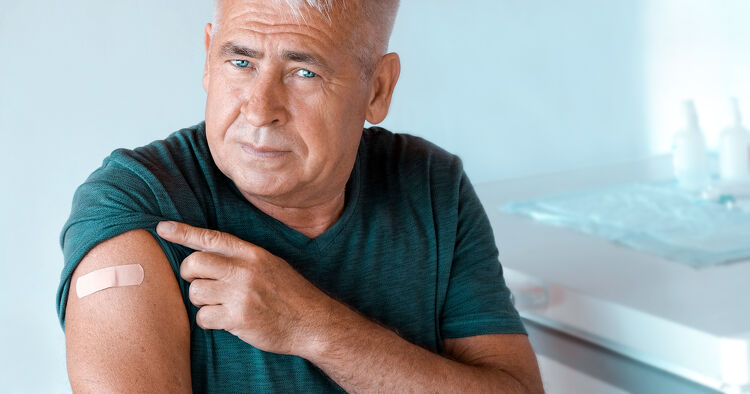 Older man pointing to a plaster on his arm after a vaccination