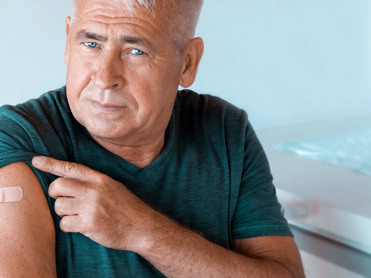 Older man pointing to a plaster on his arm after a vaccination