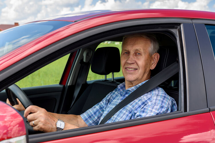 Older man smiling while sitting in the driver's seat of a car