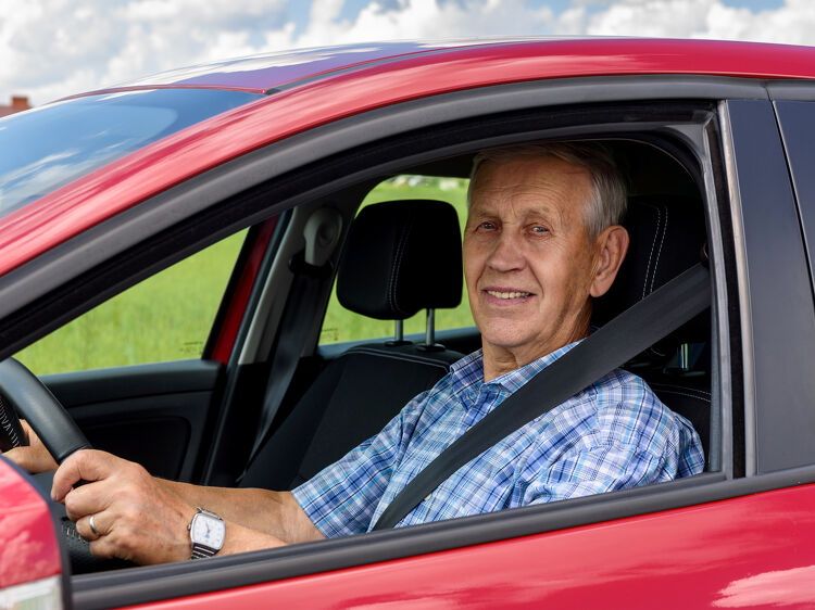 Older man smiling while sitting in the driver's seat of a car
