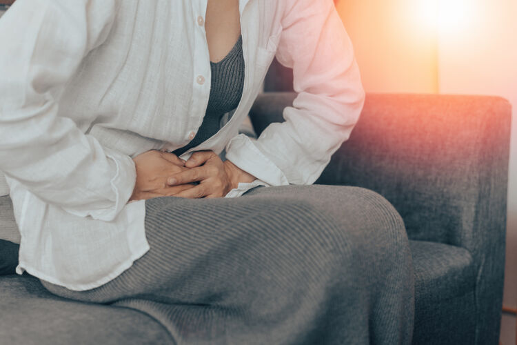 Woman sitting on a couch holding her abdomen in pain