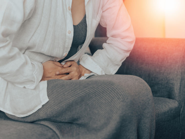 Woman sitting on a couch holding her abdomen in pain