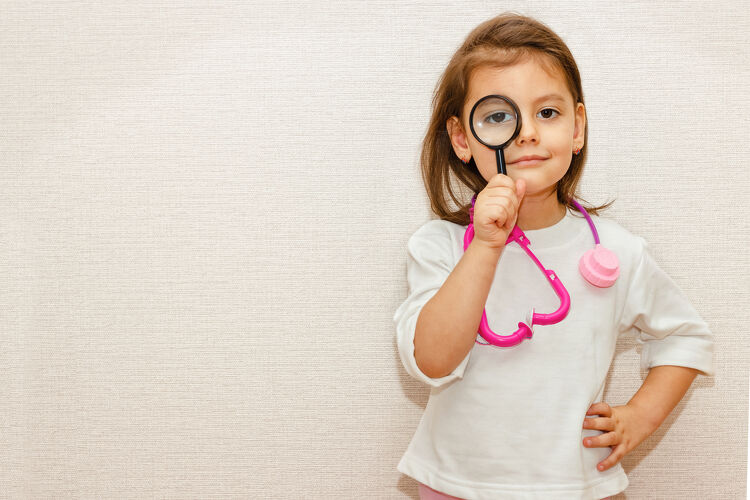Young girl in a toy stethoscope looking through a magnifying glass