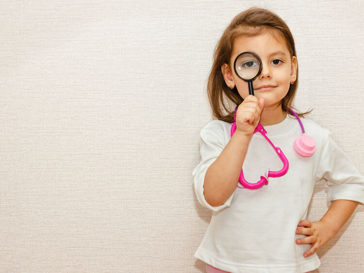 Young girl in a toy stethoscope looking through a magnifying glass