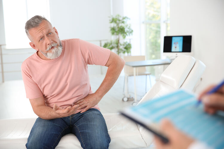 Older man sitting on exam table holding his side in discomfort