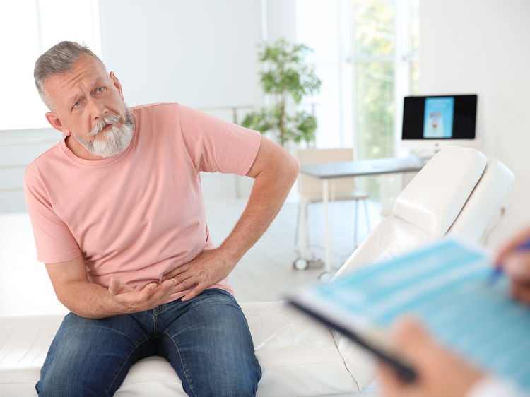 Older man sitting on exam table holding his side in discomfort